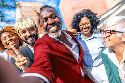 Люди різного віку, раси та статі щиро усміхаються на тлі будівлі